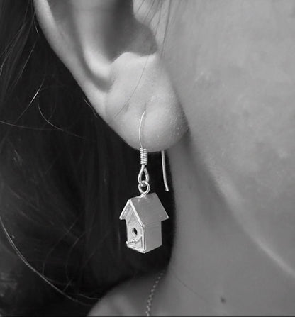 Close-up of a person wearing silver birdhouse earrings.