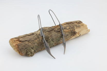 Oxidised silver phoenix feather drop earrings on a piece of wood in studio