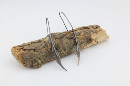 Oxidised silver phoenix feather drop earrings on a piece of wood in studio