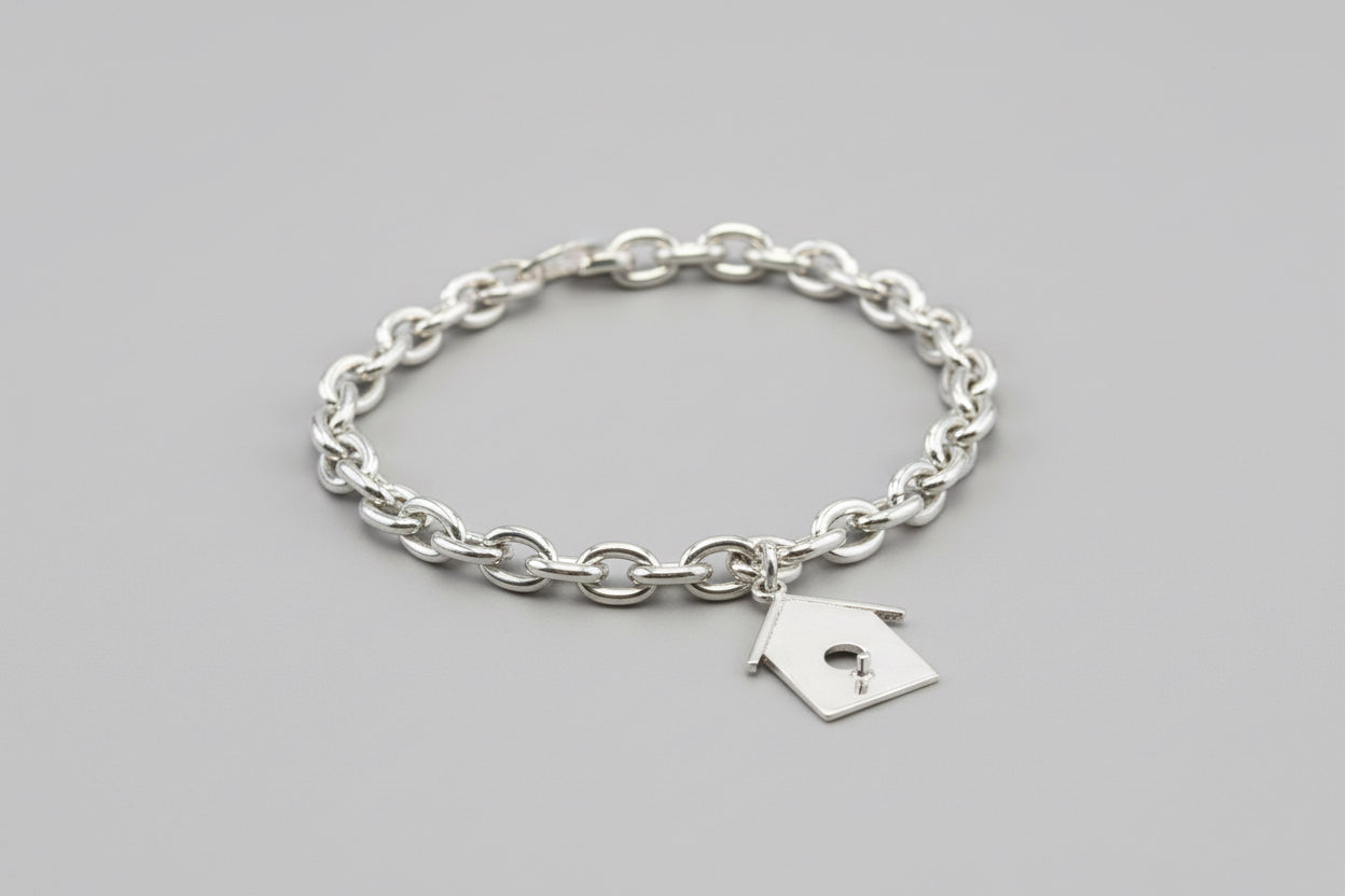 Silver chain bracelet with a small birdhouse charm on a bed of moss.