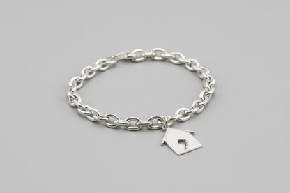Silver chain bracelet with a small birdhouse charm on a bed of moss.