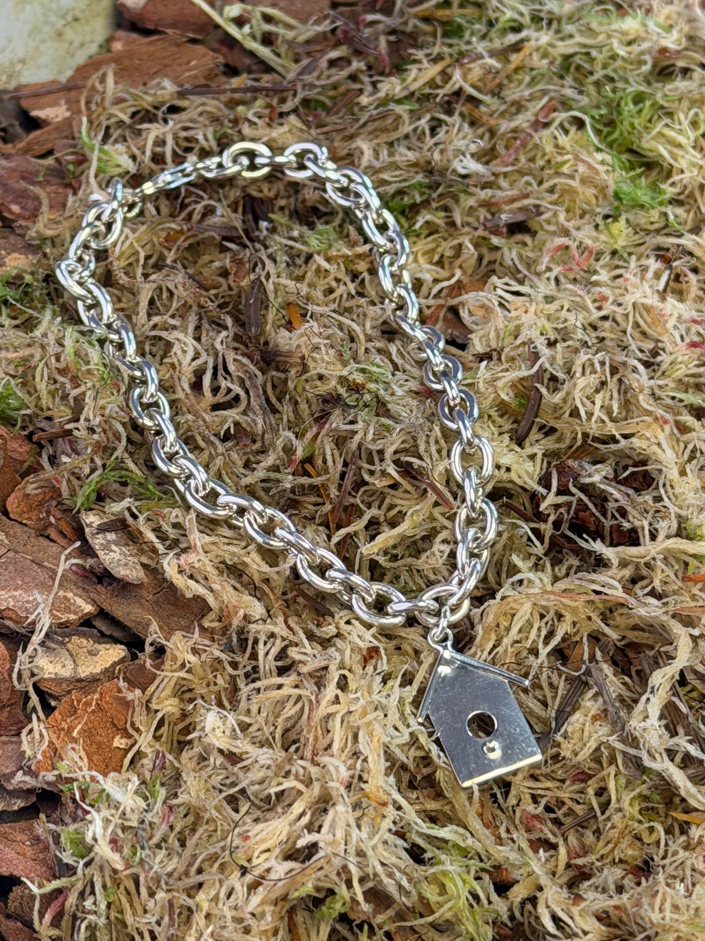 Silver chain bracelet with a birdhouse charm on a natural background