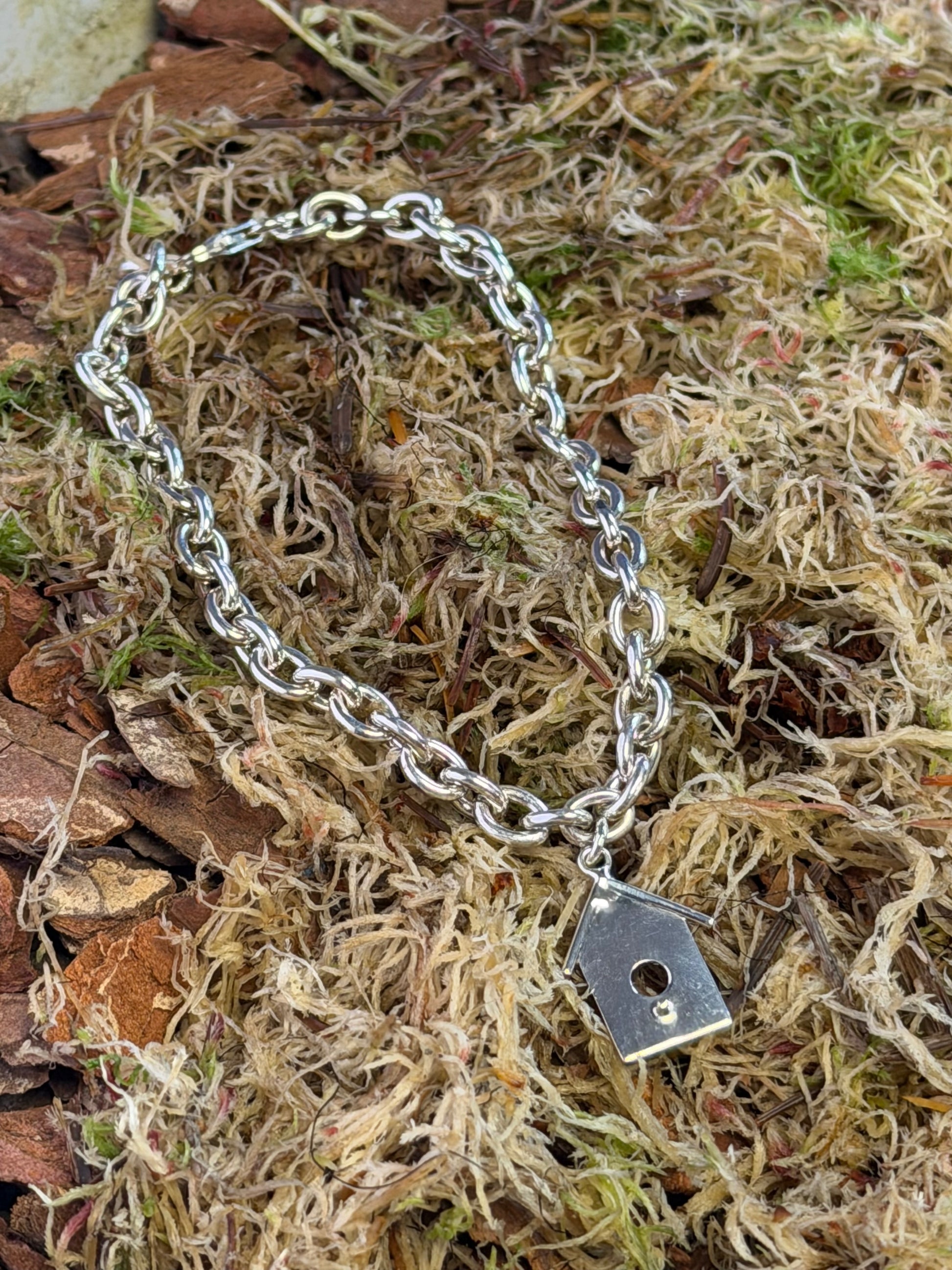 Silver chain bracelet with a birdhouse charm on a natural background