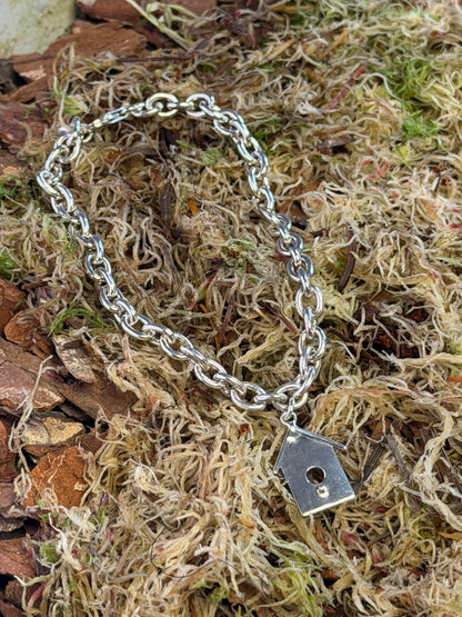 Silver chain bracelet with a birdhouse charm on a natural background