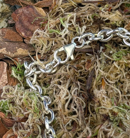 Silver chain bracelet on a natural background of moss and wood.