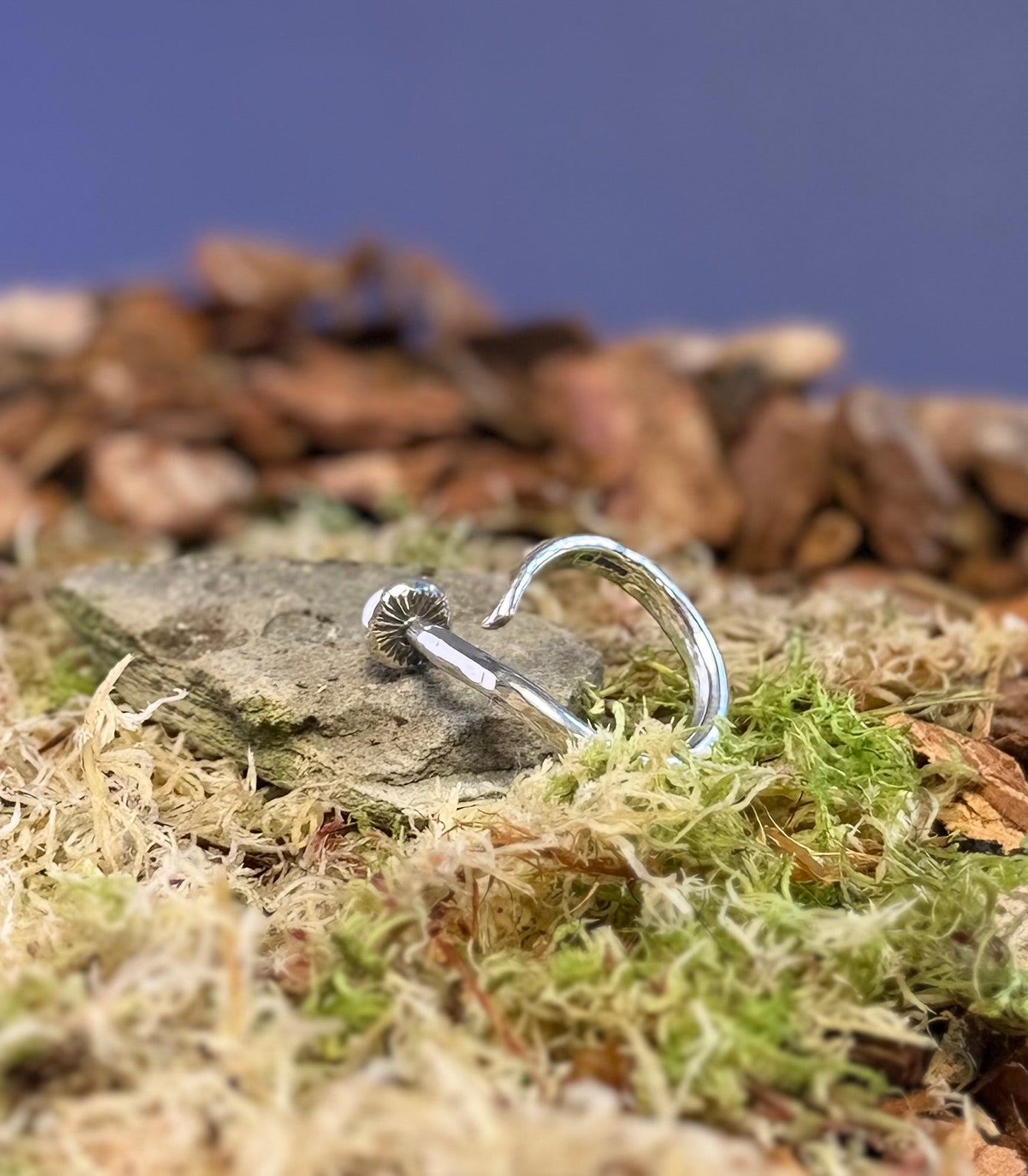 Silver mushroom ring on a stone with moss and wood chips in the background