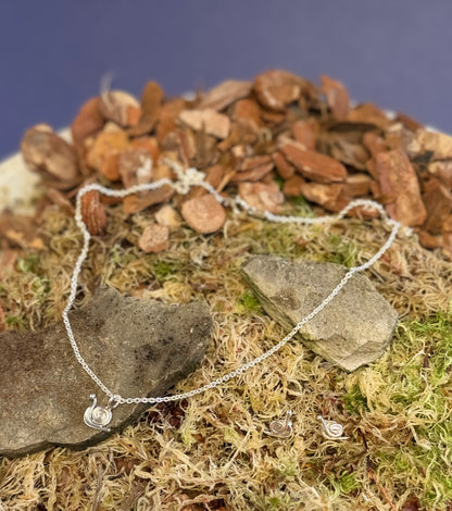Silver necklace with a snail pendant and matching earrings on a rock and moss background
