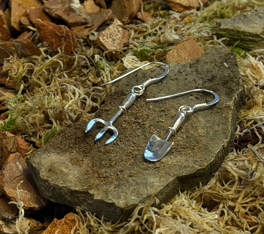 Silver fork and shovel earrings on a stone surface with natural background