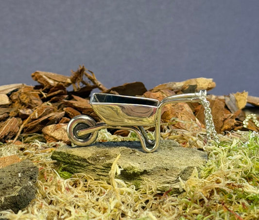 Small silver wheelbarrow charm on a natural background with rocks and moss.