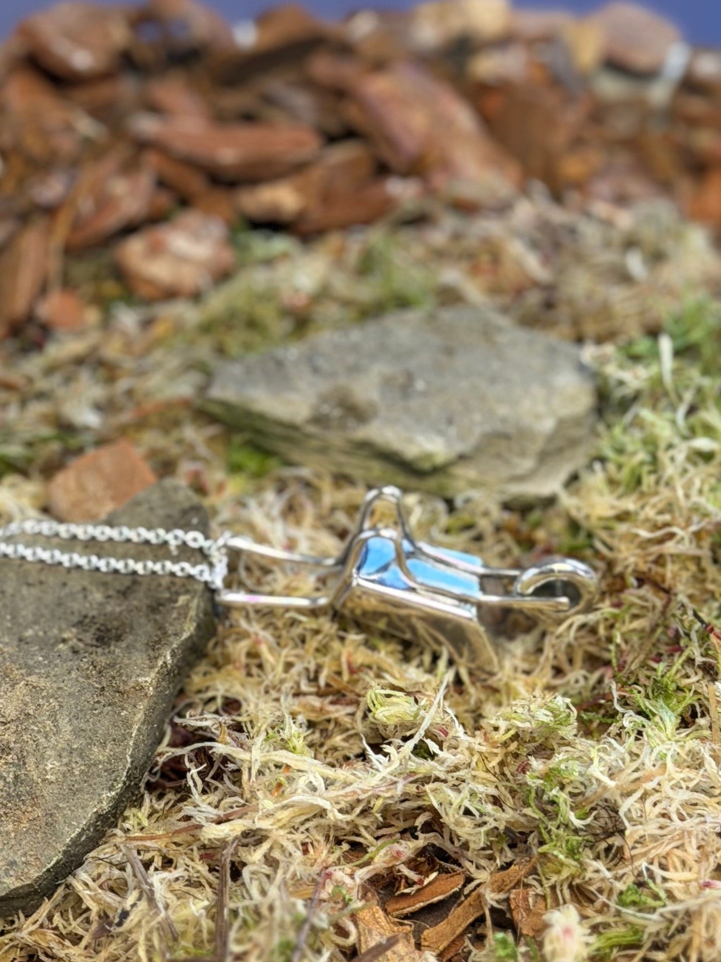 Silver necklace with a wheelbarrow pendant on a natural background of stones and moss
