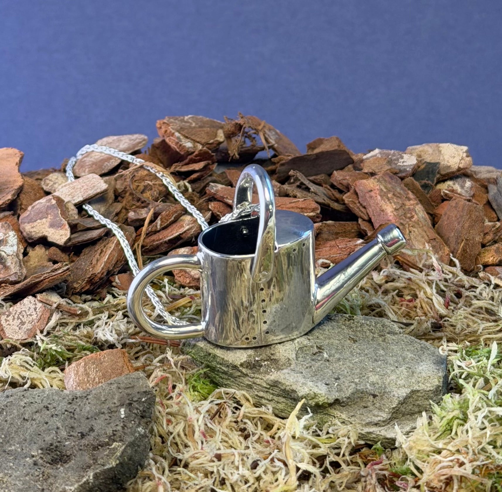 Silver watering can pendant on a rocky and natural background