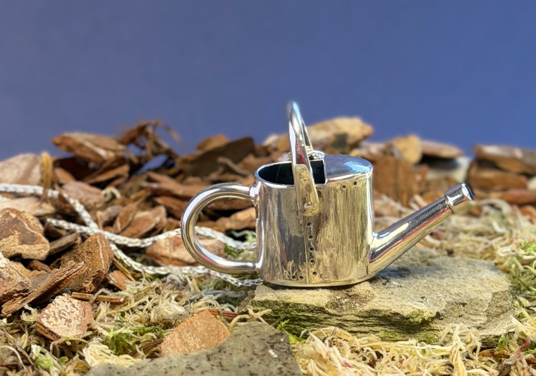Silver watering can on a natural background with wood chips and straw.