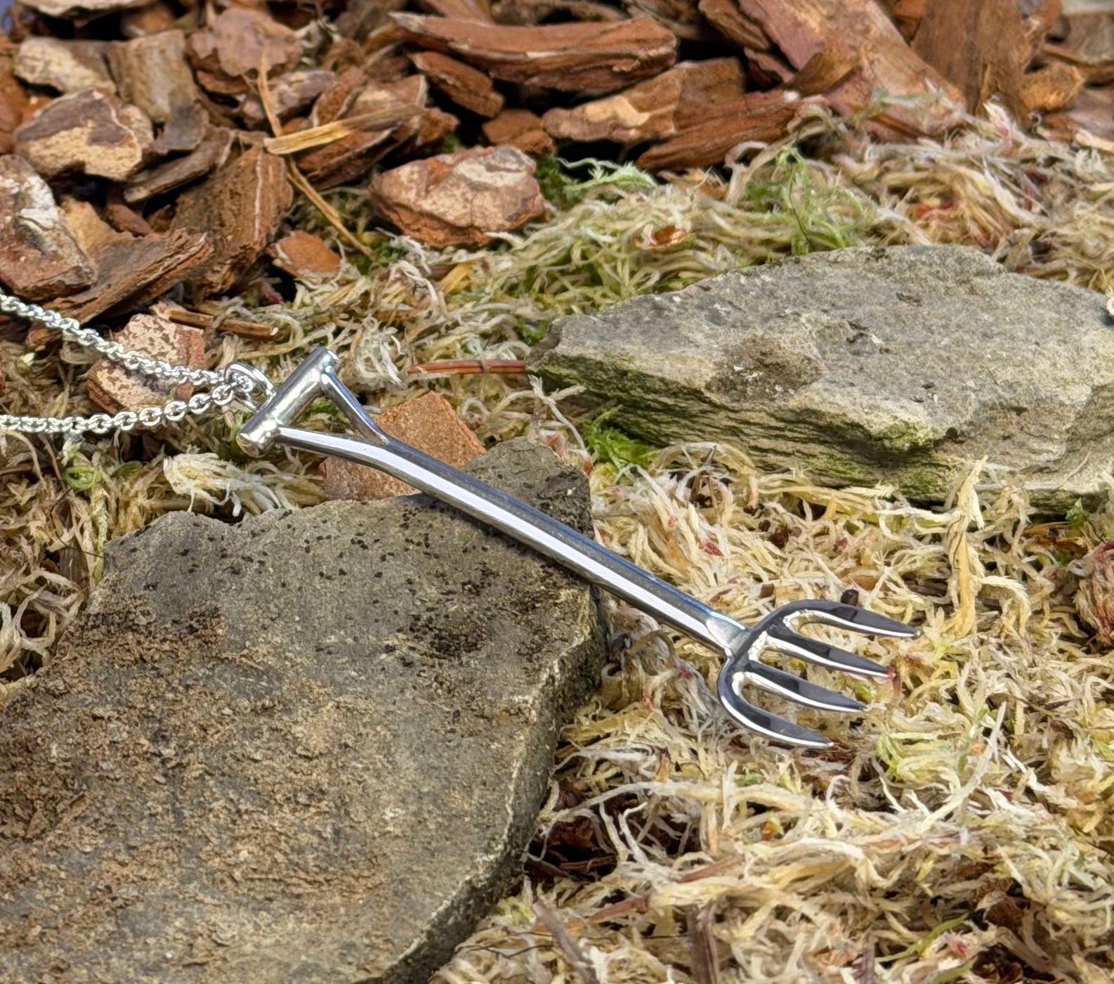 Silver garden fork-shaped necklace on a natural background with rocks and moss