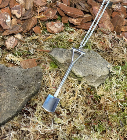 Spade shaped pendant on a chain lying on a natural ground with stones and moss.