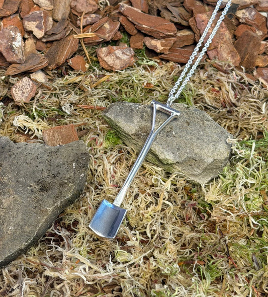 Spade shaped pendant on a chain lying on a natural ground with stones and moss.