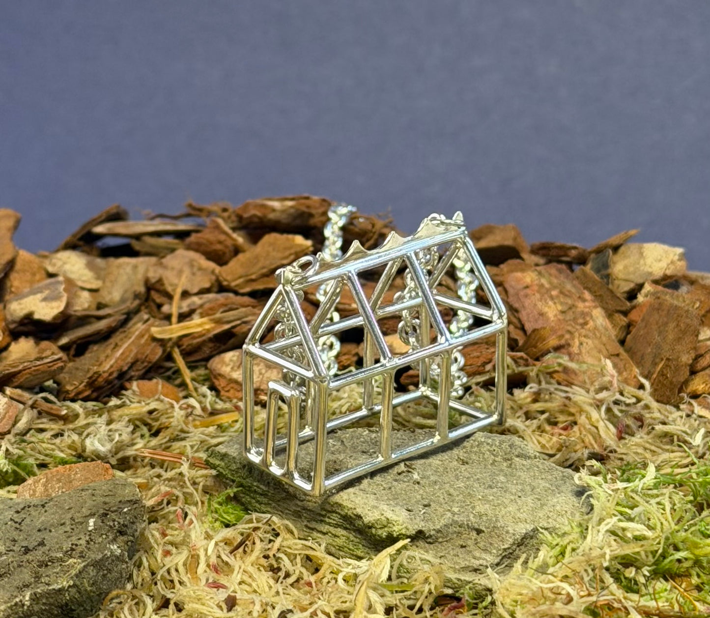 Small silver Greenhouse model pendant on a natural background