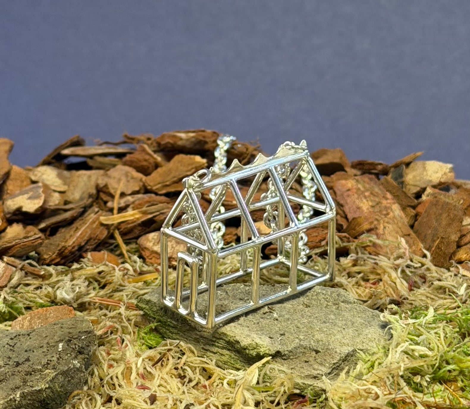 Small silver Greenhouse model pendant on a natural background