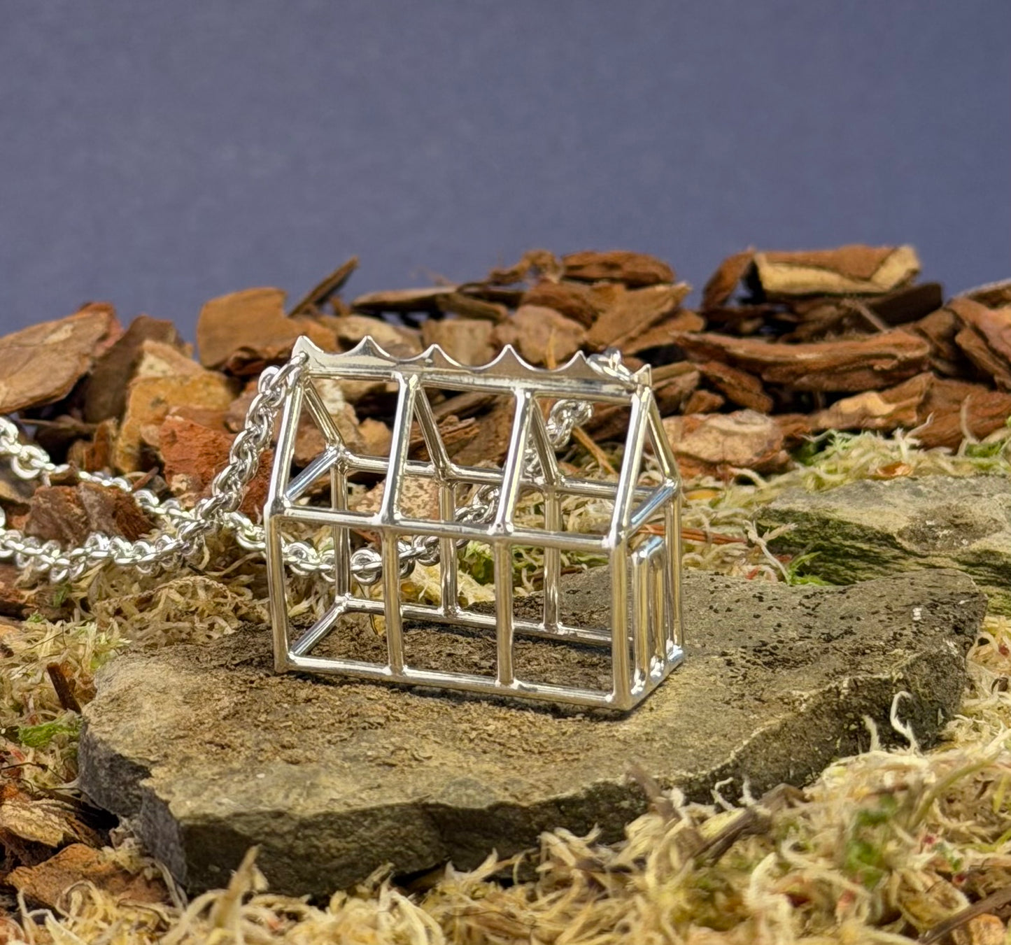 Silver miniature Greenhouse pendant on a chain against a natural background