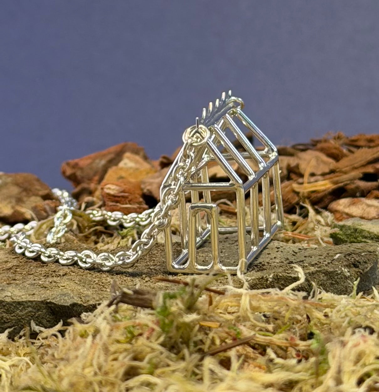 Silver Greenhouse shaped pendant on a chain against a natural background