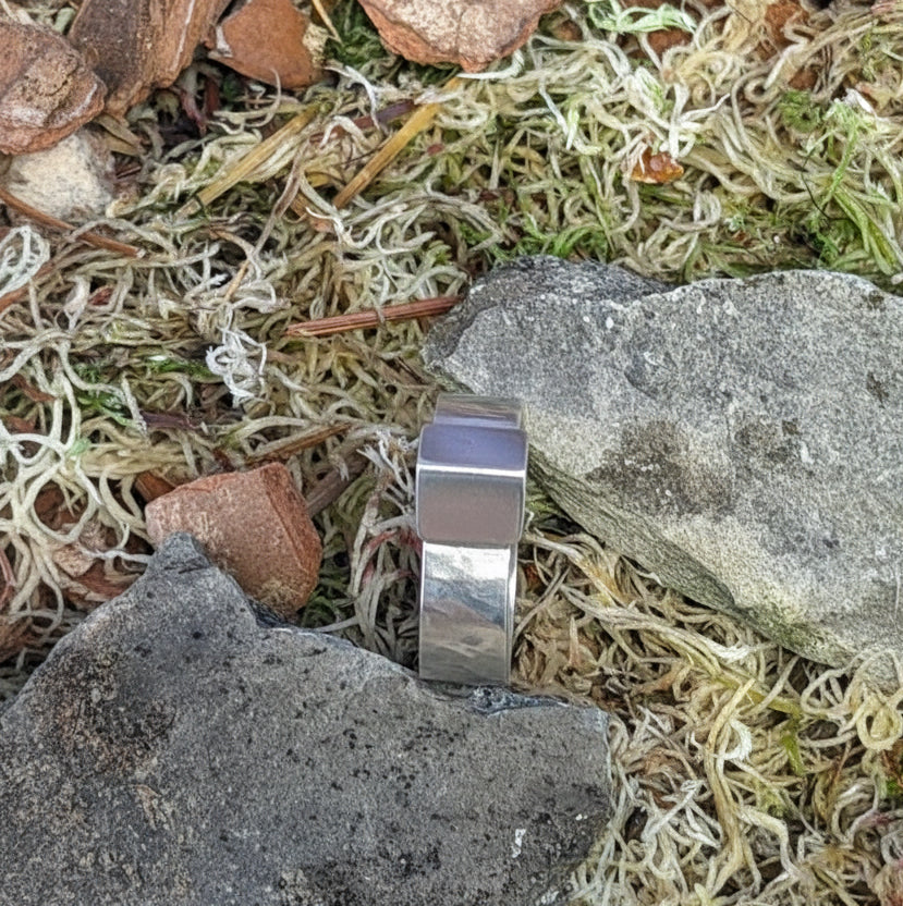 silver ring on a stone surface with moss and small stones.