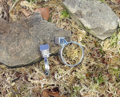 Two silver rings on a natural background with stones and moss.