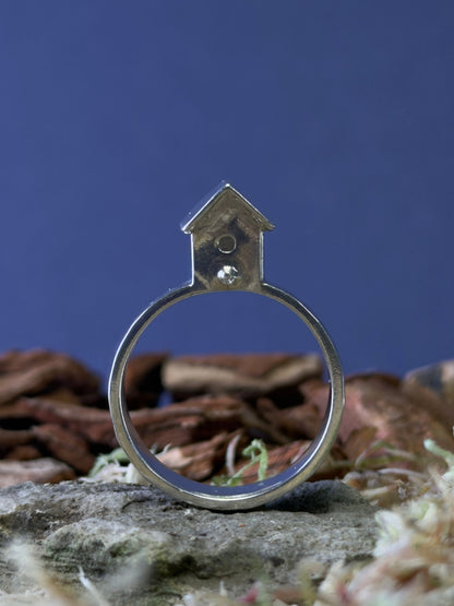 Silver ring with a small birdhouse shaped top on a natural background
