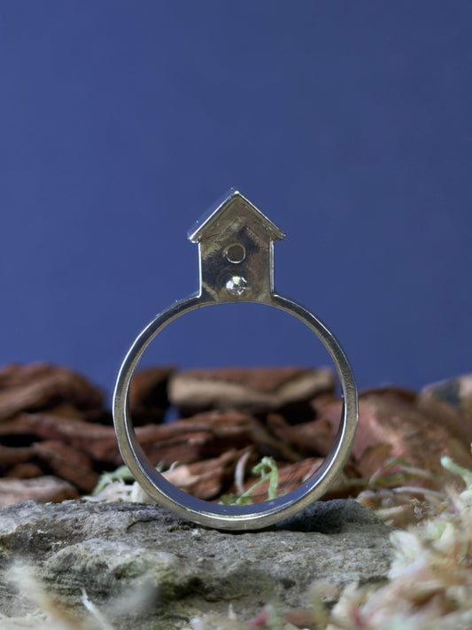 Silver ring with a small birdhouse shaped top on a natural background