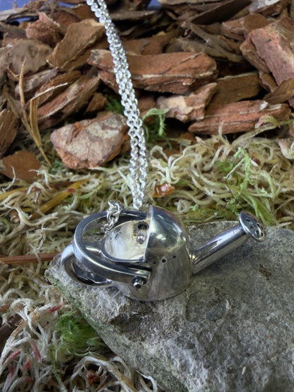 Silver necklace with a watering can pendant on a stone and moss background