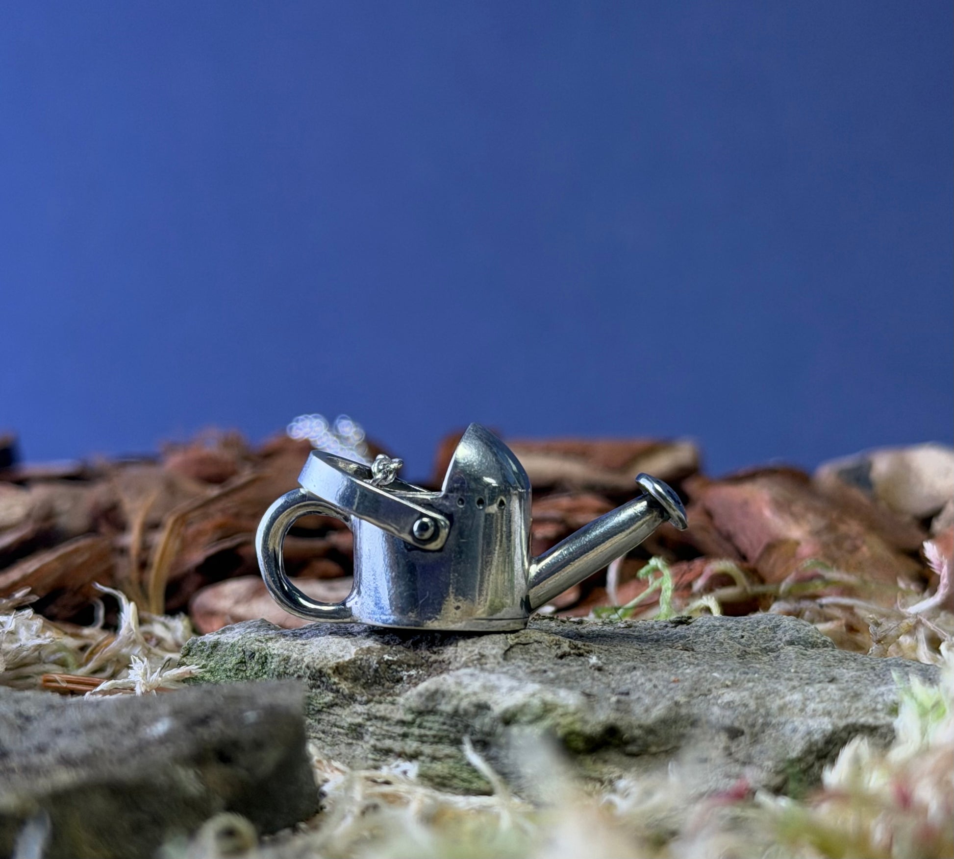 Silver watering can shaped pendant on a natural background