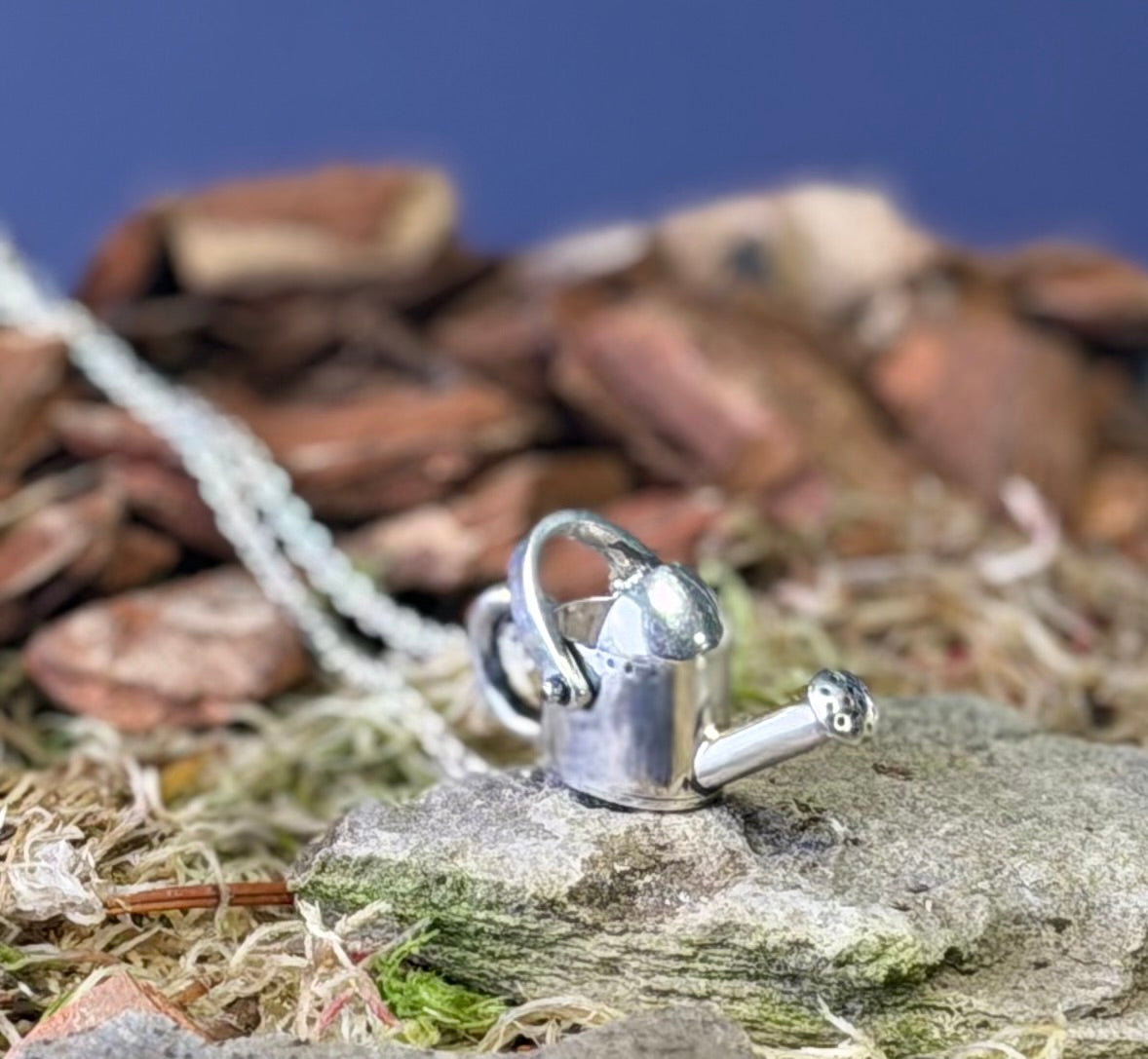 Silver watering can charm on a rock with a natural background