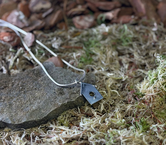 Necklace with a small birdhouse shaped pendant on a stone and moss background