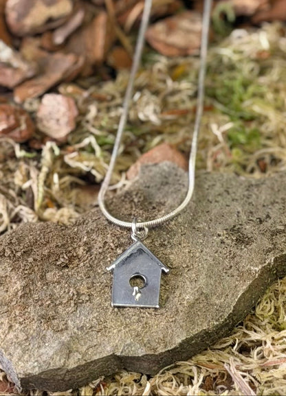 Silver necklace with a birdhouse pendant on a stone surface with natural background