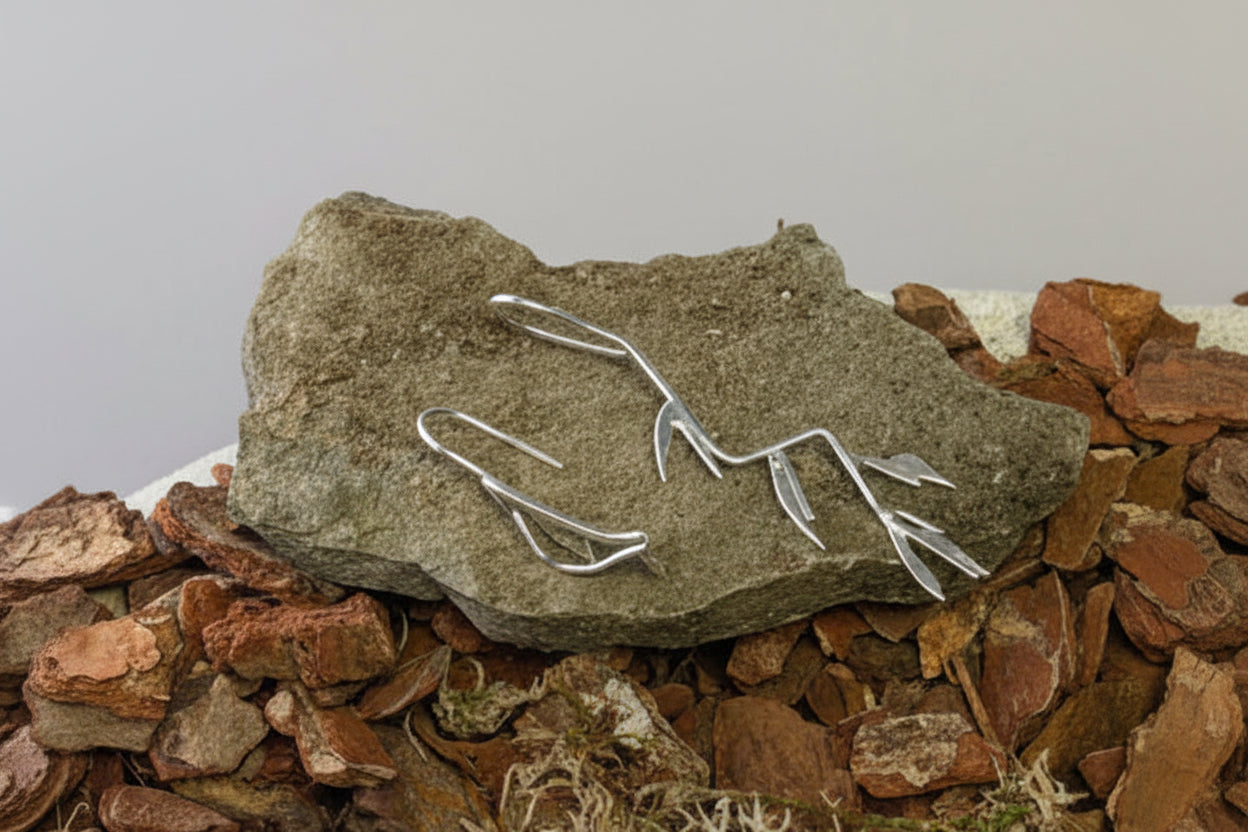 Bird and branch earrings on slate with wood chips and moss surrounding them