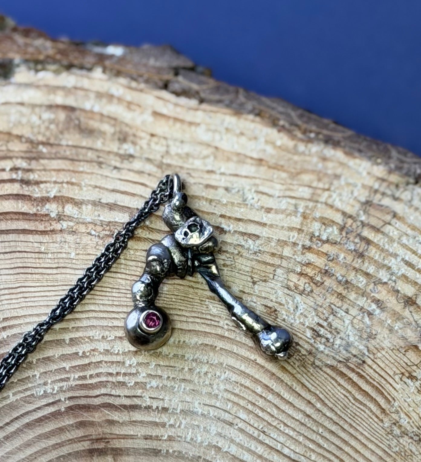 Silver skeleton key pendant with a pink gemstone on a chain, placed on wooden surface.