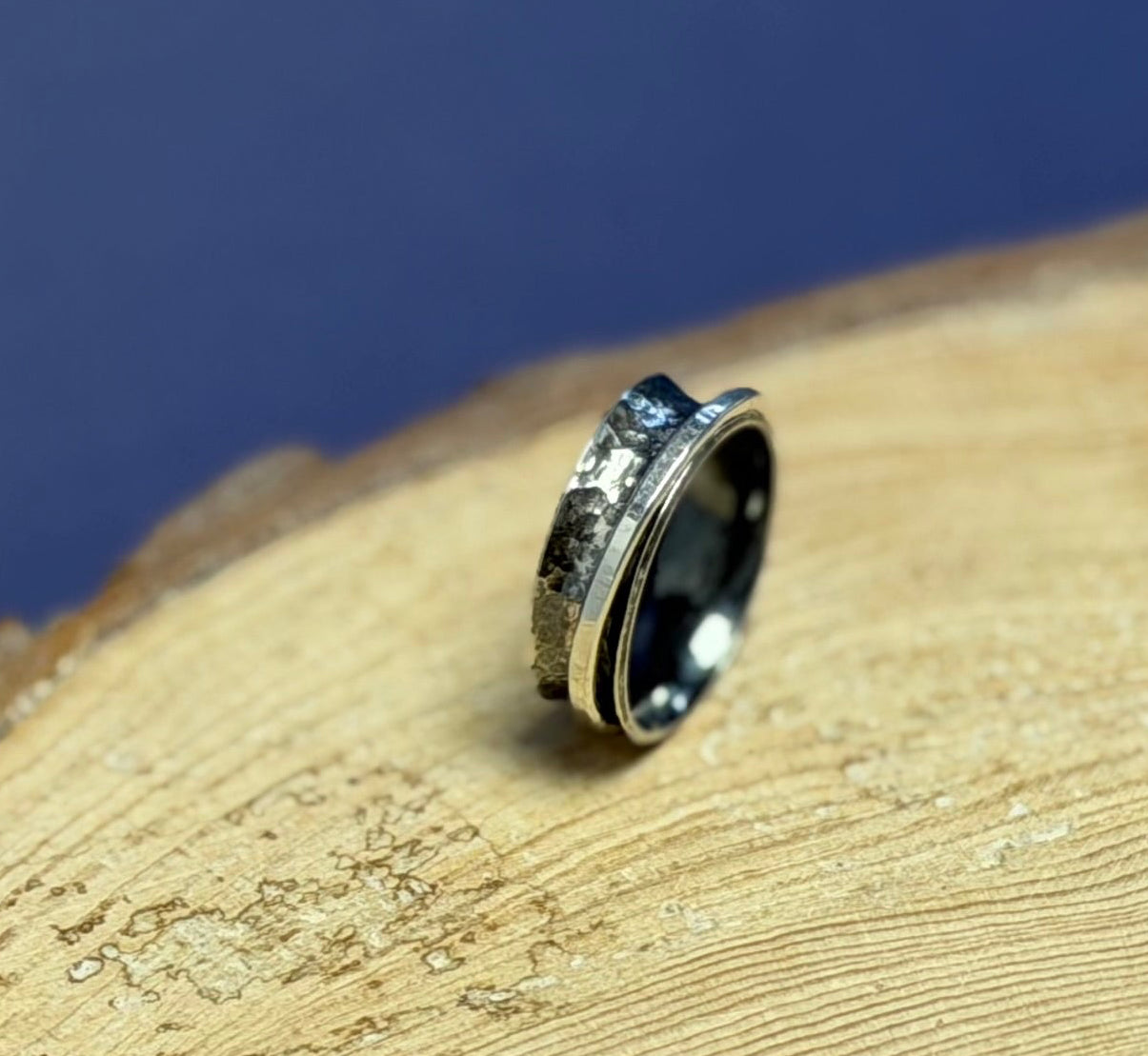 Silver hammered oxidised spinner ring on a wooden surface with a blue background