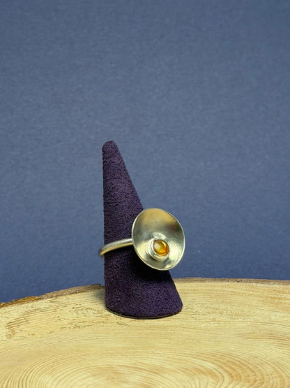 Silver ring with a central Amber gemstone on a purple cone against a blue background