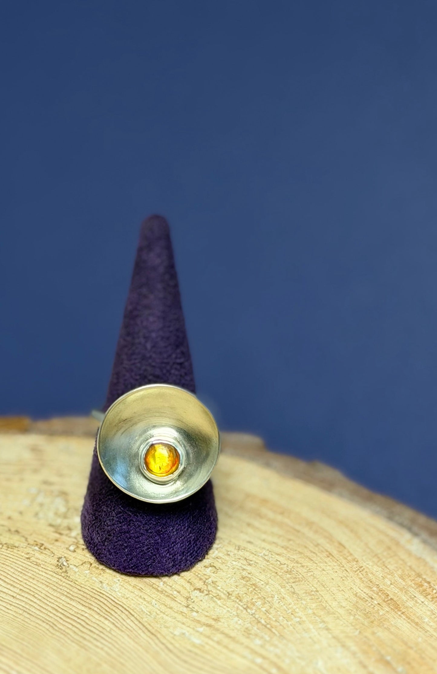 Silver ring with dome, set with an Amber stone on a purple cone against a blue background