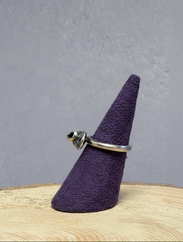 Purple cone-shaped ring holder with a silver ring on a wooden surface and blue background