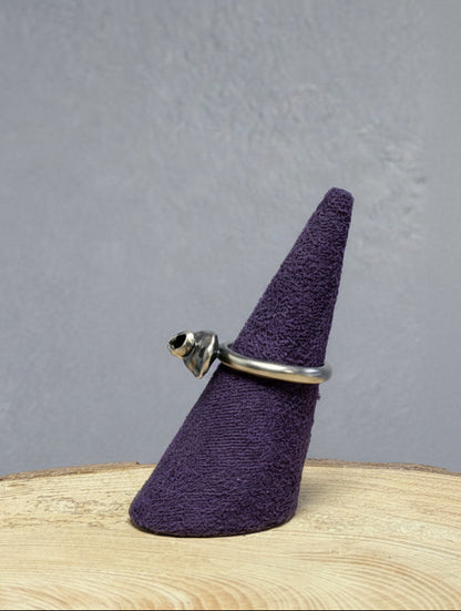 Purple cone-shaped ring holder with a silver ring on a wooden surface and blue background