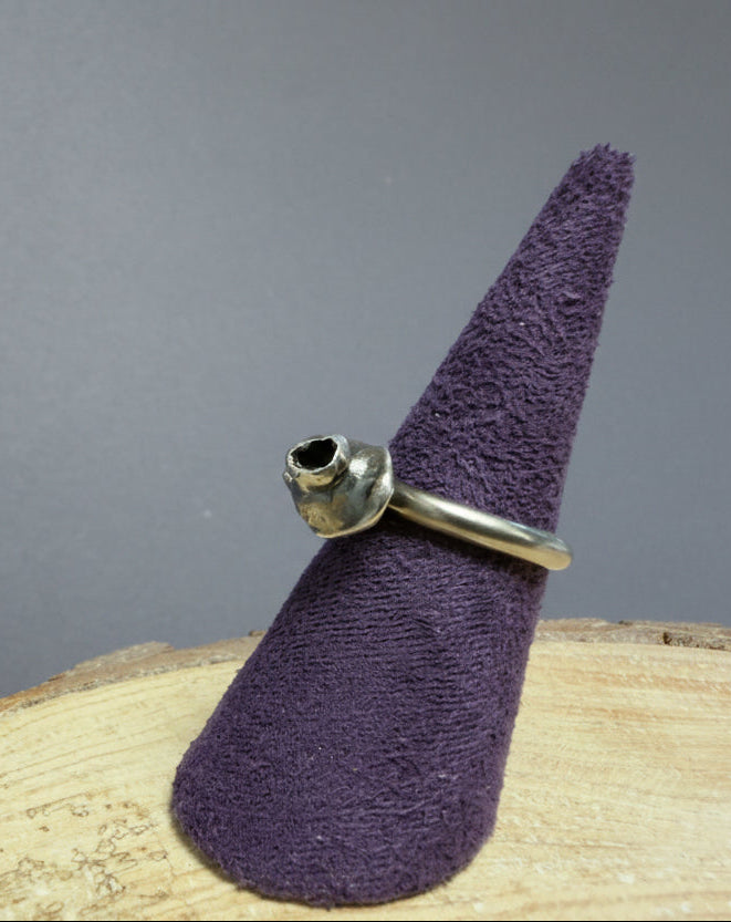 Purple cone-shaped object with a silver oxidised ring on a wooden surface against a blue background