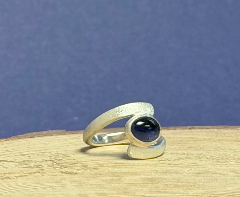 Silver ring with an Iolite gemstone on a wooden surface with a blue background