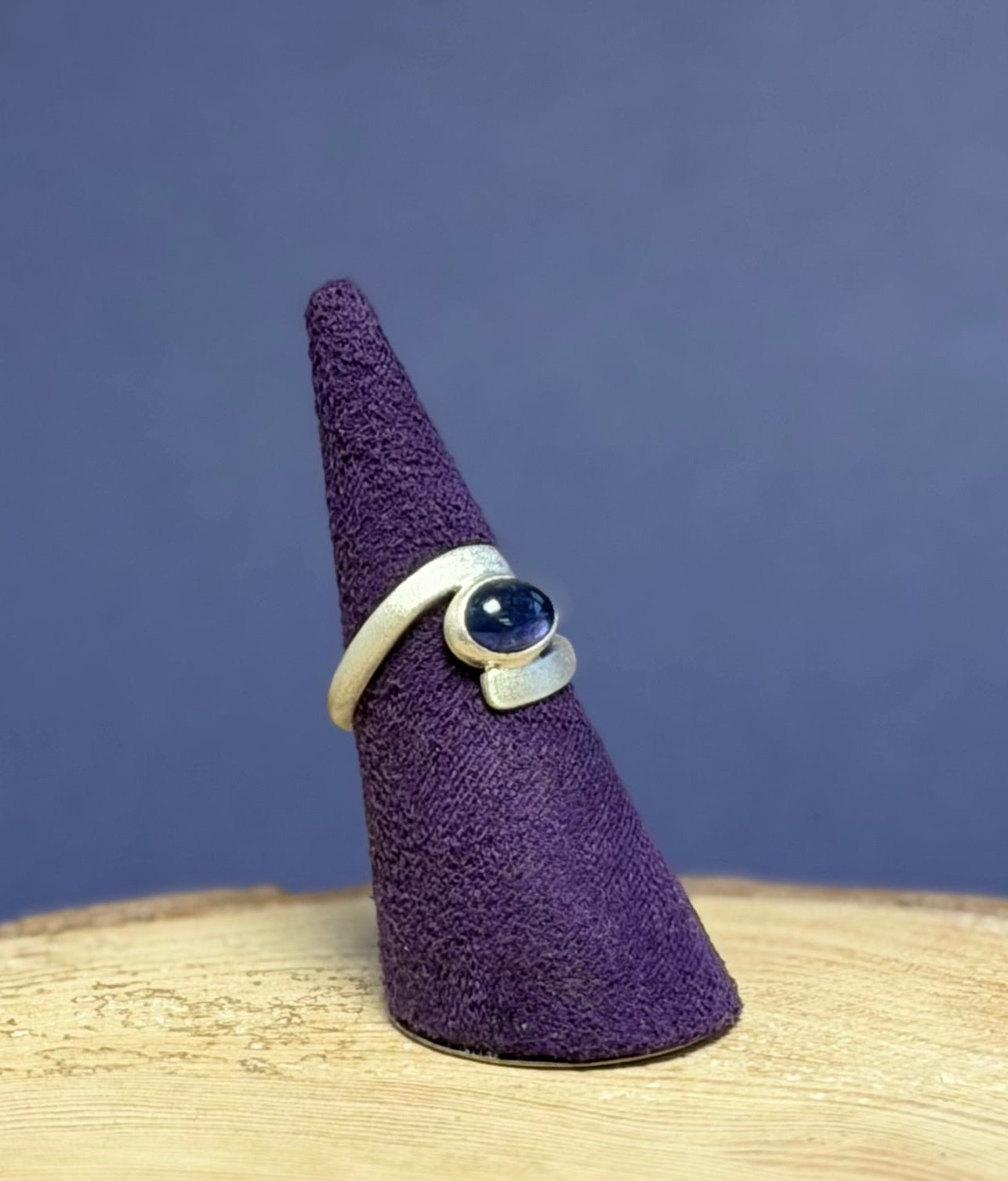 Ring with a blue purple gemstone on a purple cone-shaped stand against a blue background