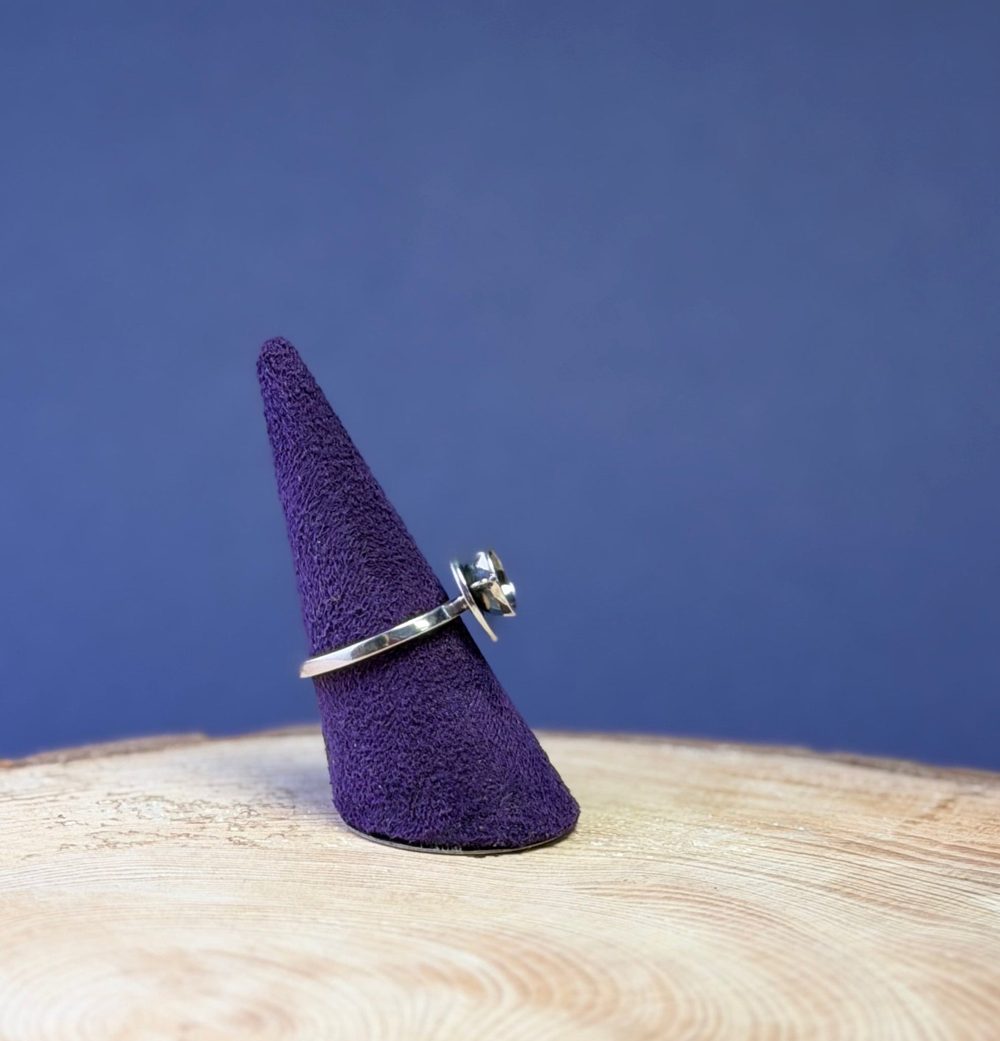 Silver teacup ring on a purple cone-shaped stand against a blue background