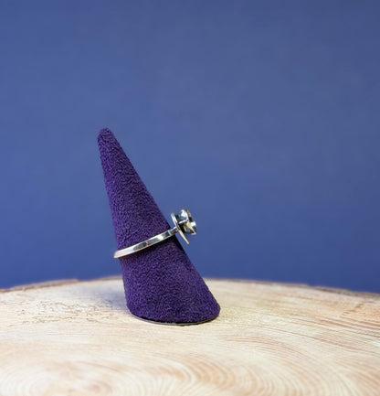 Silver teacup ring on a purple cone-shaped stand against a blue background