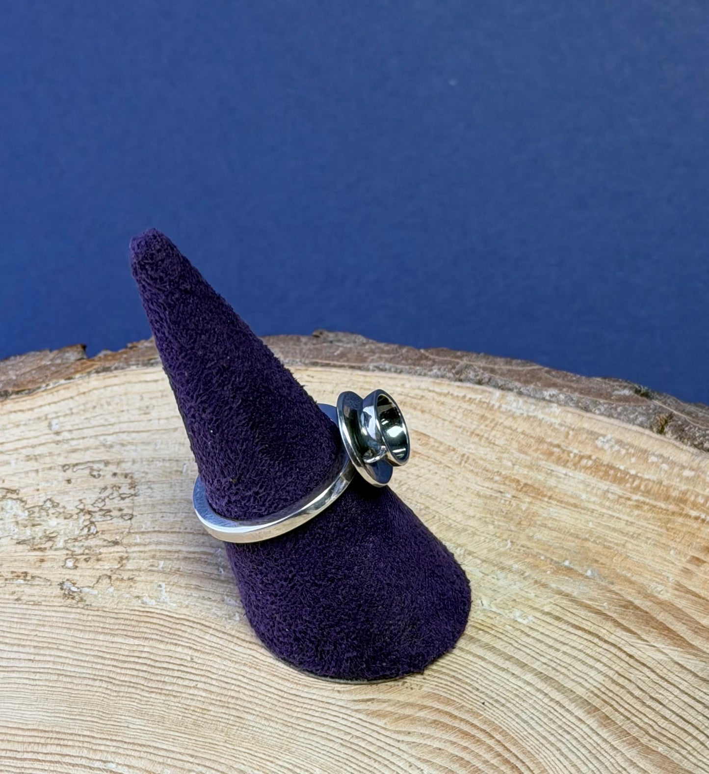 Purple pointed ring mount with a teacup ring on a wooden surface with a blue background