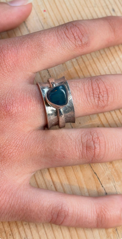 Close-up of the green-blue stone spinner ring worn on a finger, showing the textured silver band and narrow spinning ring.