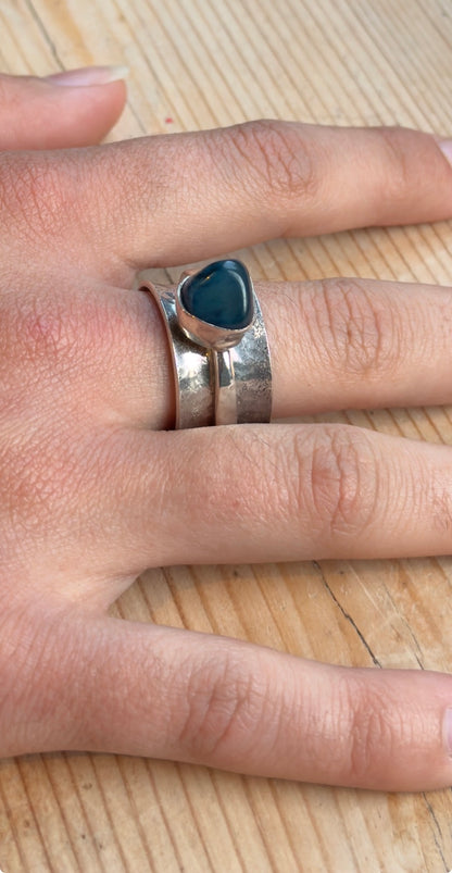 Angled view of the sterling silver spinner ring worn on a hand, showing its raised green-blue stone setting and hammered band.