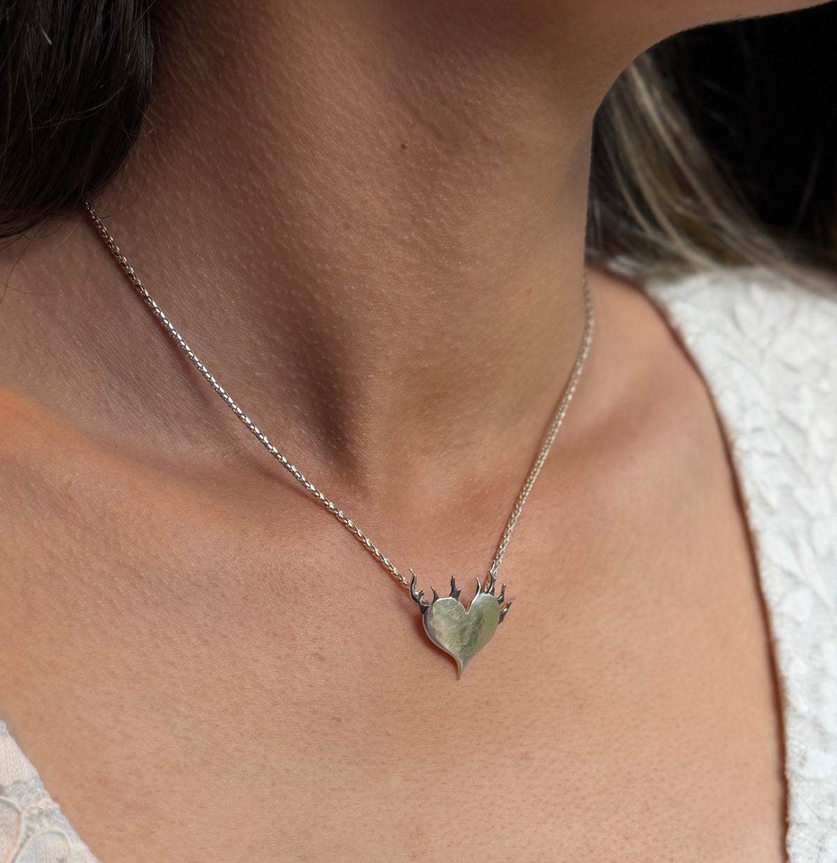 Silver Love Set on Fire heart pendant worn on a fine chain, showing its satin finish and flame-shaped details.