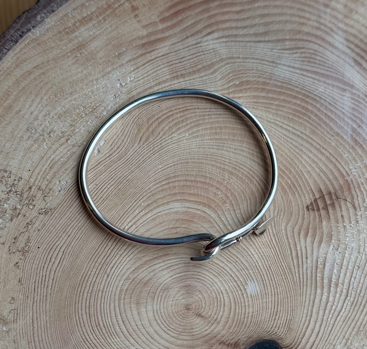 Silver bangle with trowel catch resting on wood