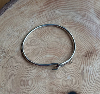 Silver bangle with trowel catch resting on wood